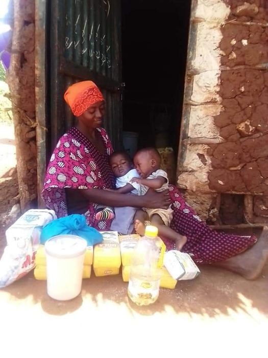 A mother holding her two young children at her doorway, with a food parcel of flour, oil and essentials from Helping Hands