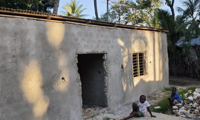 A new cement-rendered house with its roof on, nearly complete, under palm trees